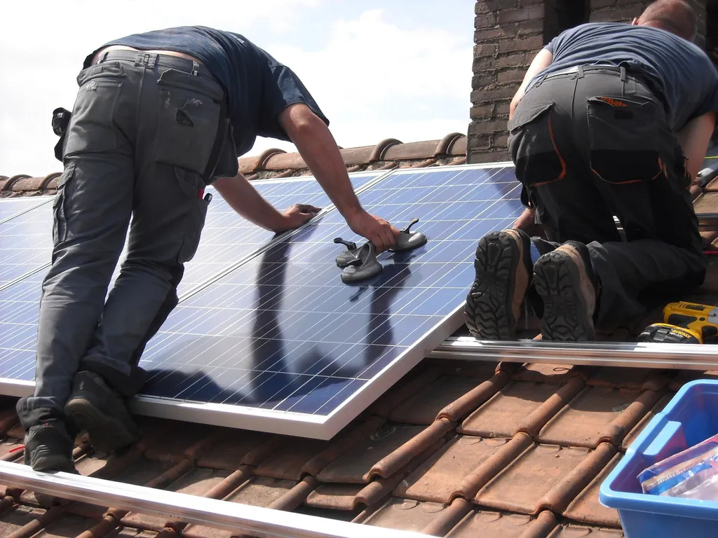 Deux poseurs fixent des modules photovoltaïques sur une toiture en tuiles
